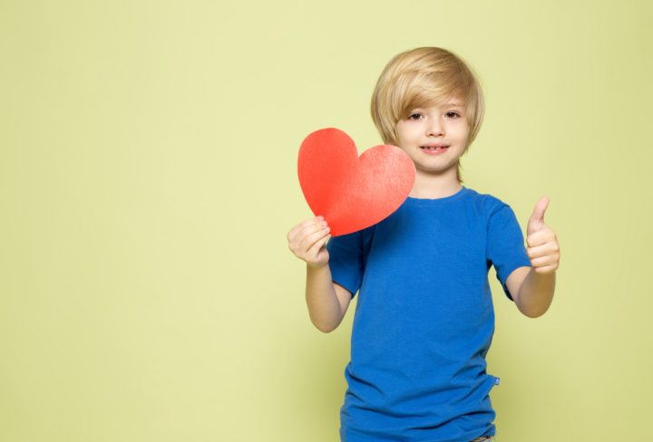 front-view-smiling-boy-blue-t-shirt-holding-heart-shaped-figure-stone-colored-space